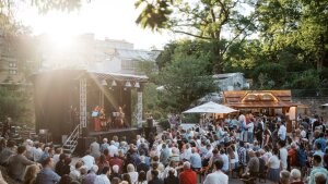 Viele Menschen stehen im Sonnenschein vor der Bühne neben den Gewächshäusern